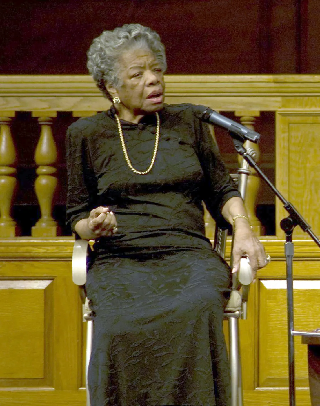 Maya Angelou seated on stage, speaking into a microphone
